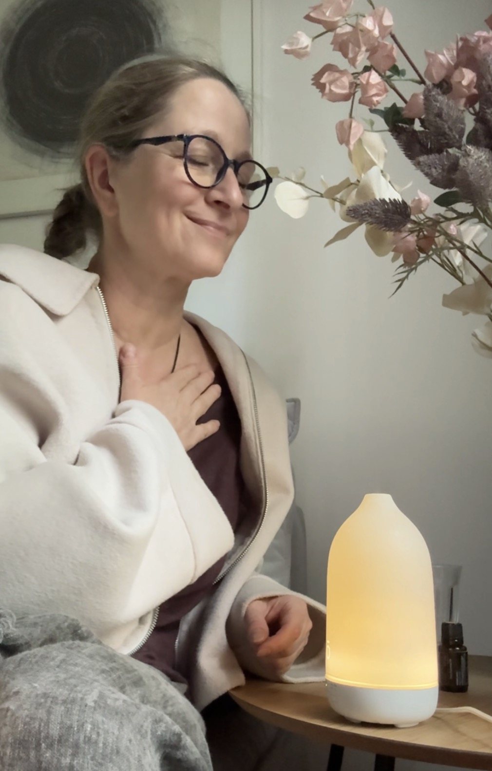 Magdalena Wangrat z zamkniętymi oczami i dłonią na sercu, obok dyfuzor i suszone kwiaty